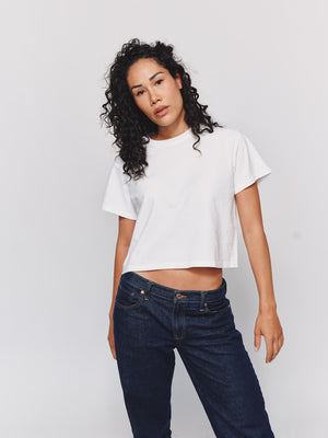 Woman wearing a white t-shirt and dark blue jeans on a plain background
