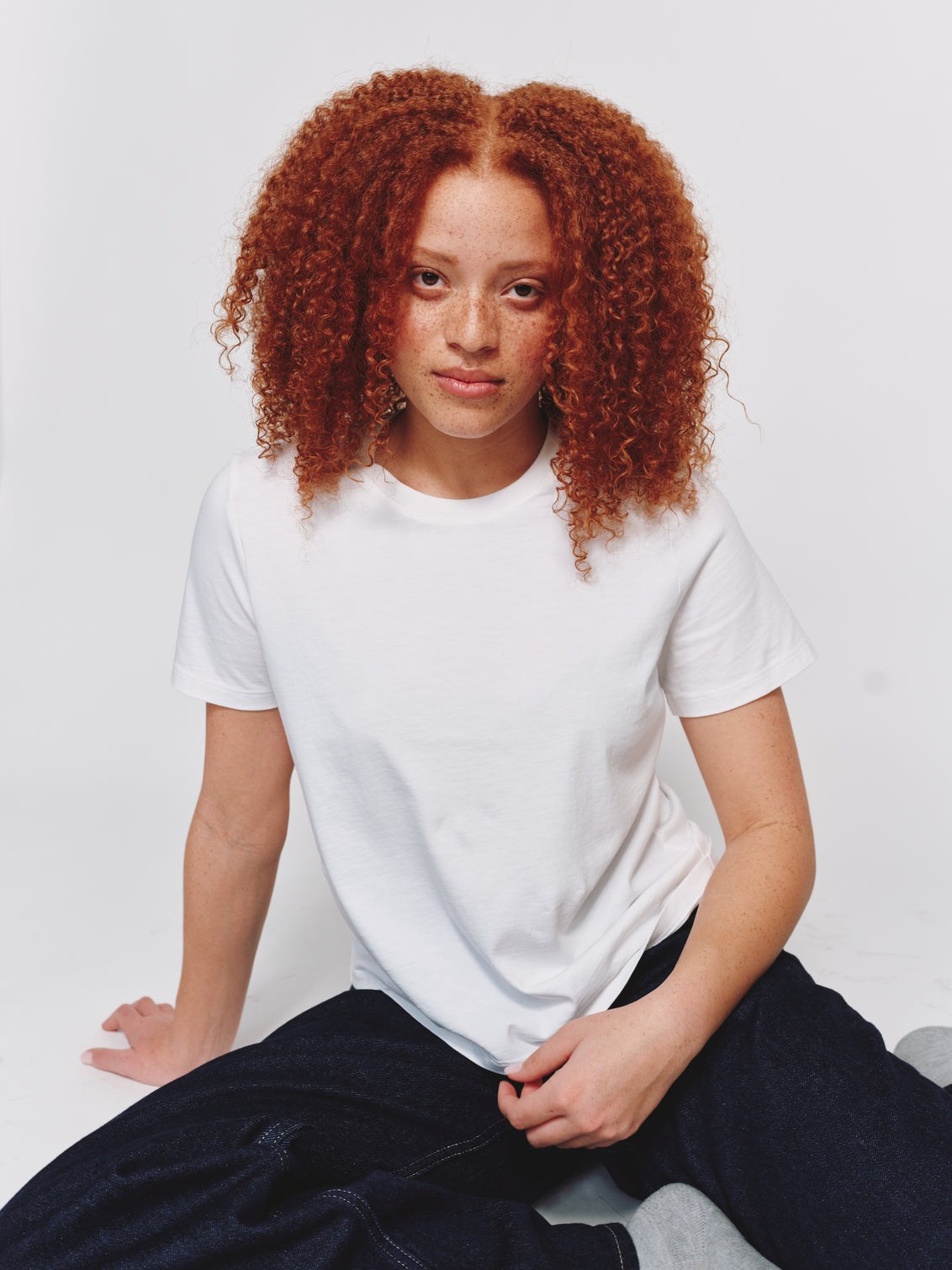 Model wearing size M in a classic-fit white t-shirt and dark denim jeans while seated against a light gray background