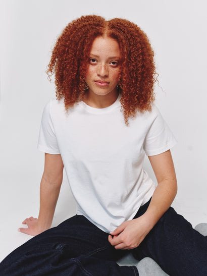 Model wearing size M in a classic-fit white t-shirt and dark denim jeans while seated against a light gray background