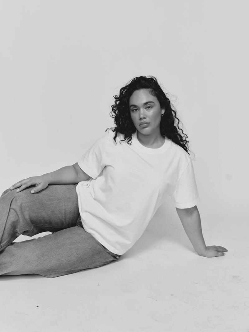 Model seated on the floor wearing the Saint Sirène Boyfriend Tee in vintage white with relaxed-fit gray trousers.